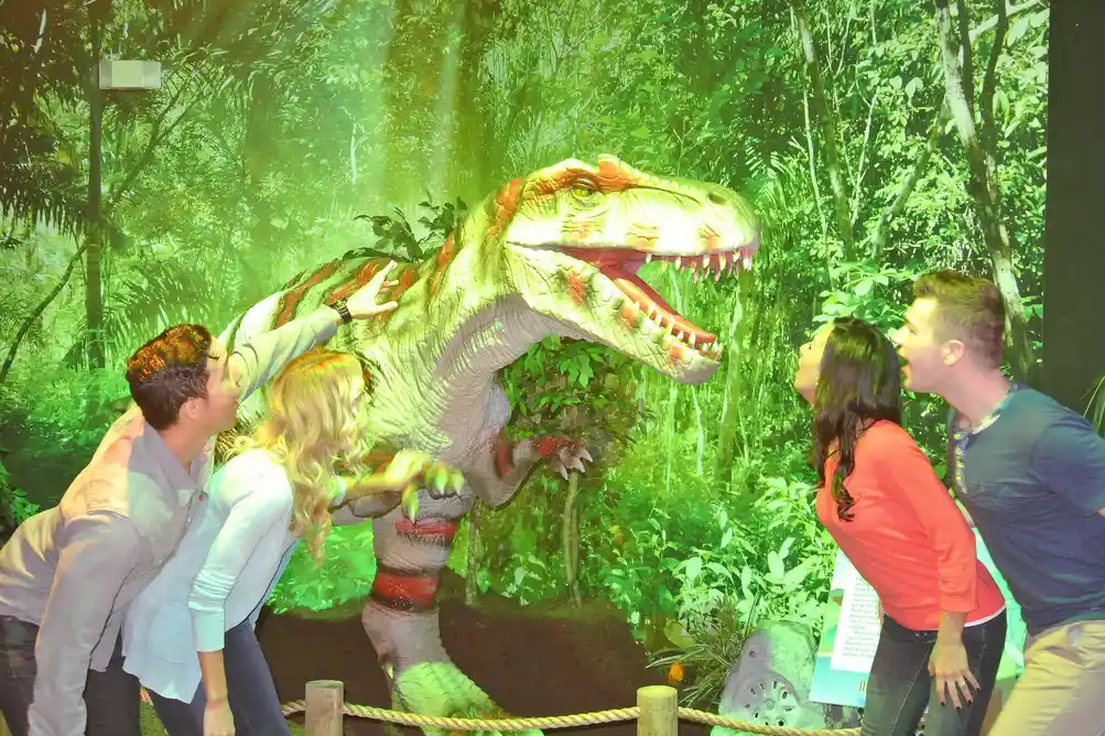 Visitors interacting with small animatronic dinosaur in commercial exhibit showing high engagement