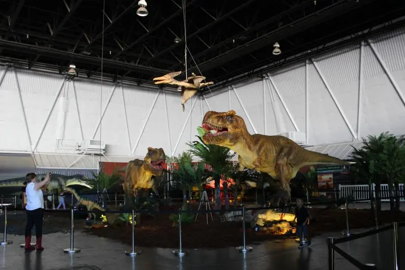 A large-scale museum dinosaur exhibit utilizing vertical space with a suspended pterosaur and ground-level animatronics, showing effective spatial planning and visitor circulation.